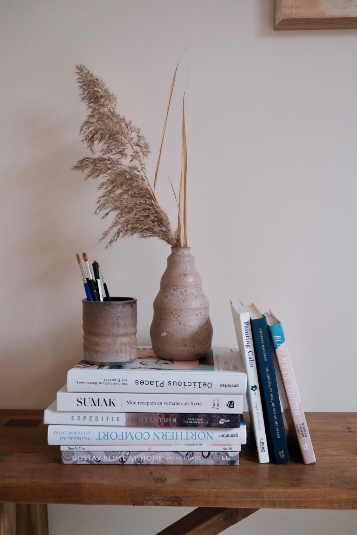 Twee abstracte schilderijen in roze tinten op een houten plank, naast een terracotta pot
